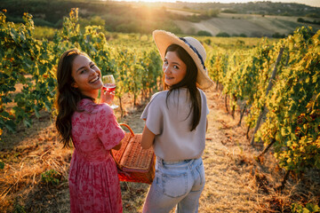 Obraz premium Two smiling female friends looking back over shoulder in vineyard