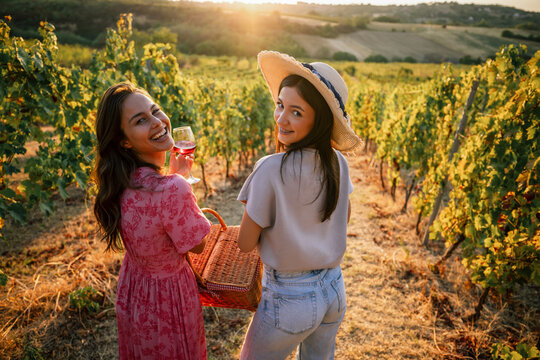 Two smiling female friends looking back over shoulder in vineyard