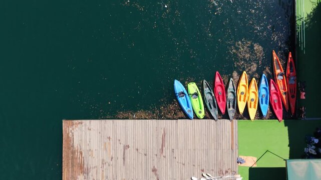 Kayaks lined up at a dock by the water in bright colors