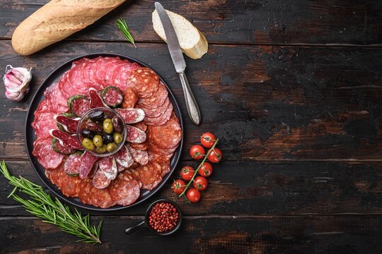 Round black ceramic platter filled with sliced spanish cured meats including chorizo salami salchichon and fuets arranged in concentric circles around a glass bowl of green