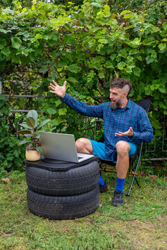 Surprised man working outdoors with laptop on stacked tires