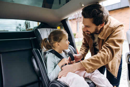 Father fastening daughter's car seat belt for travel safety