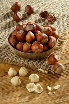Raw whole hazelnuts in shell in a wooden bowl with peeled nuts on a rustic wooden table