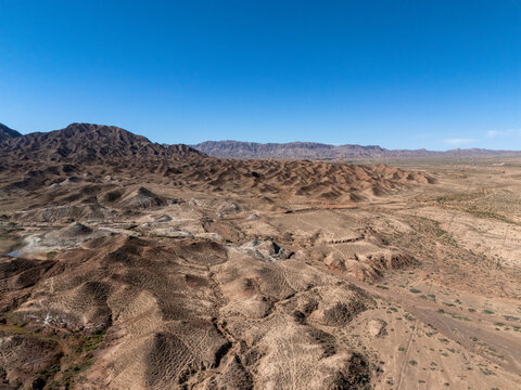 Aerial view of rolling barren desert hills and rugged terrain under clear blue sky