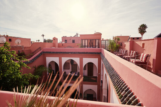 Aerial view of a traditional Moroccan riad with orange walls and green accents, surrounded by lush greenery under a clear blue sky.