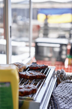 Juicy grilled steaks and burgers sizzling on a tabletop grill beside a mustard bottle, evoking backyard barbecue vibes, casual cooking and summertime outdoor meals with cozy, savory atmosphere.