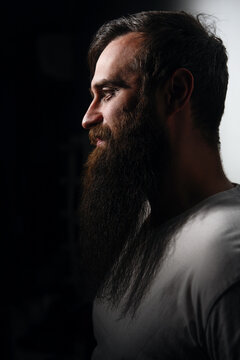Side profile portrait of bearded man in dramatic lighting against dark background.