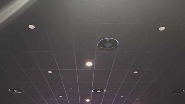 Low angle view of a modern suspended ceiling with square tiles, integrated air conditioning vents, and recessed led lighting fixtures