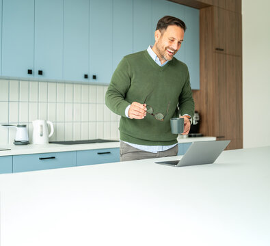 Professional man working remotely from kitchen, enjoying a video call or online meeting with coffee and eyeglasses, managing his business and accounting tasks