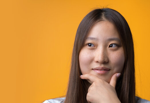 Thoughtful Young Chinese Woman Resting Hand on Chin Against Yellow Background