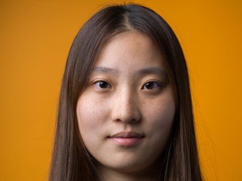 Frontal Portrait of Young Chinese Woman with Natural Freckles on Yellow Background