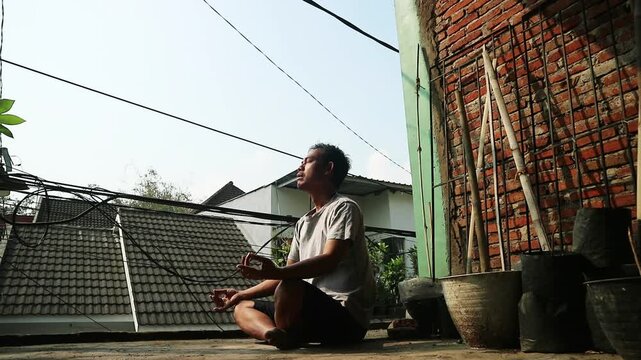 Man meditating outdoors in a relaxed pose, enjoying a peaceful moment in an urban setting.
