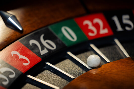 White ball in green zero pocket on wooden casino roulette wheel. Photo highlights excessive betting consequences and risk analysis topics.