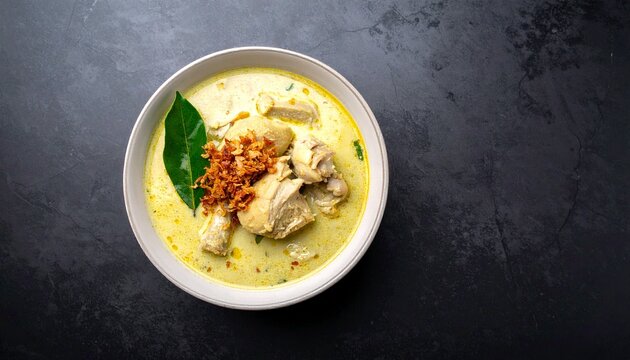 Creamy Thai Yellow Chicken Curry in a White Bowl with Fried Garlic and Kaffir Lime Leaf on Dark Background