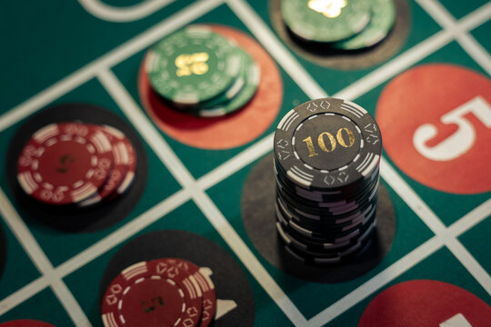Tall stack of black one hundred casino chips on green roulette table. Photo shows the danger of gambling addiction and excessive betting risk.