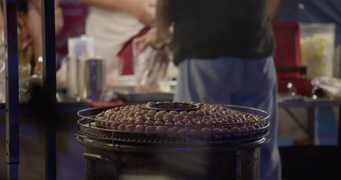 Close-up of grilled sausage skewers arranged on a round stove at a night market. Warm lighting and street food atmosphere in Thailand.