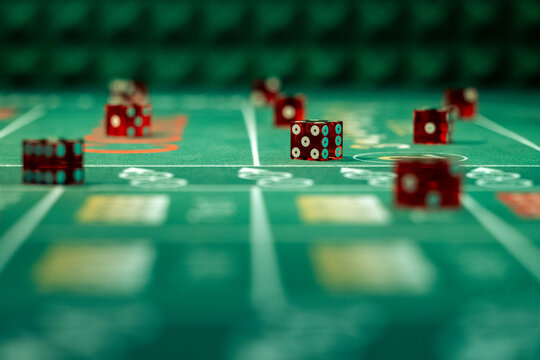 Red casino dice on green craps felt table in low angle view with pyramid bumper wall. Asset for casino promotions, gambling nights, and tabletop tournaments.