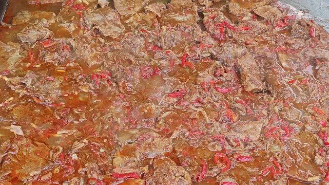 a large batch of a braised or stewed meat dish, resembling a beef stew or goulash cooked with sliced red peppers and onions in a rich, reddish-brown gravy.