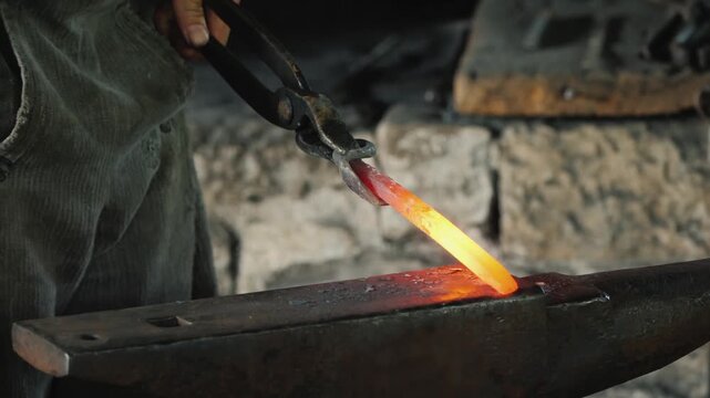 Blacksmith shaping hot metal on anvil with hammer in traditional forge footage.