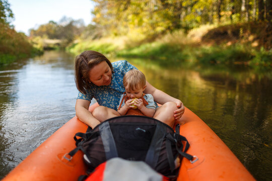 Mother looking at her infant child under one year old eating an apple in an orange kayak on water