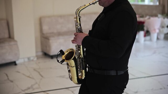 Musician in black clothing playing a golden saxophone during a live performance at an elegant indoor event or celebration.