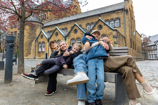 Women girlfriends children enjoy playful break bench autumn city trip near historic architecture. Candid travel scene shows family fun, friendship, tourism, leisure, bonding and joyful togetherness