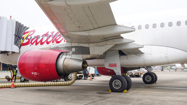 Batik Air Airbus A320 parked at Hang Nadim International Airport in Batam, Indonesia, showing jet engine, landing gear, wing, and jet bridge during ground handling before flight preparation.