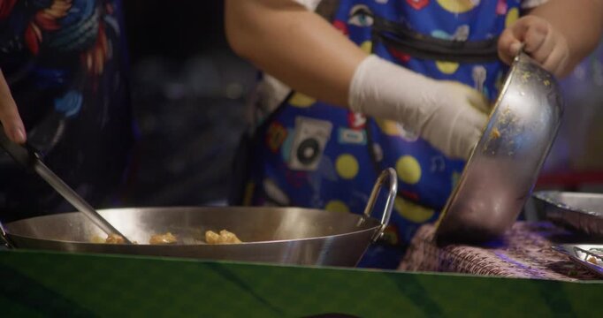 Street food vendor shaping and preparing Thai fish cakes from minced fish mixture at a night market stall. Close-up of hands working with ingredients in an outdoor setting.
