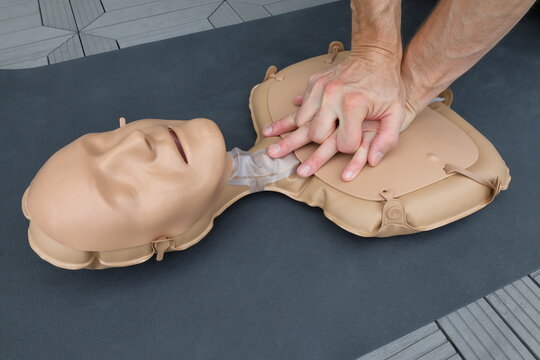 CPR or cardiopulmonary resuscitation practice on a dummy doll. Male arms and hands visible. First aid concept.