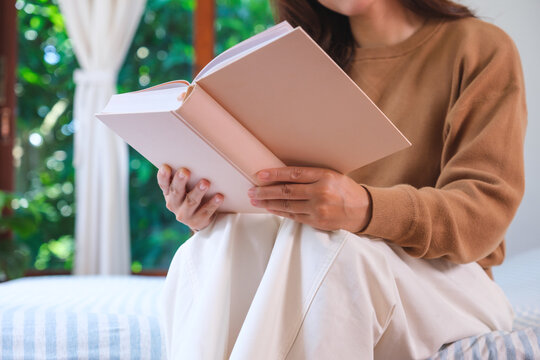Closeup image of a woman reading a book on the bed at home