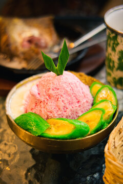 Traditional Indonesian es pisang ijo shaved ice dessert with green banana and syrup in coconut bowl top view for culinary concept