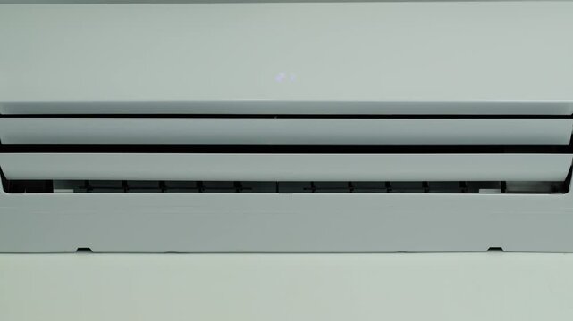 Close up of white air conditioner with digital display showing 21 degrees Celsius, louvers moving.