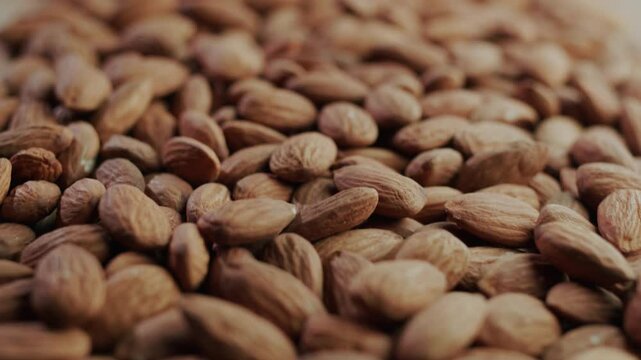 Slow motion camera movement over pile of raw almond nuts on wooden background with organic texture.