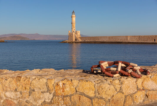 Historic Venetian lighthouse and stone harbor wall illuminated by warm sunrise light in Chania, Crete, Greece.
