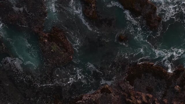 Dramatic aerial views reveal the rugged, rocky coastline of Kelecung Beach, with turquoise whirlpools, foaming waves and tidal pools creating a textured seascape and a strong atmospheric feel