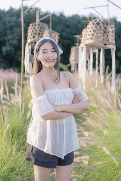 Beautiful young Asian woman in a white dress posing in a tall grass field decorated with bamboo lanterns in nature, wearing a headscarf during sunny outdoor leisure travel vacation in a scenic landsca