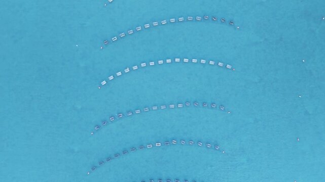 Aquaculture oyster farm top-down aerial view showing floating cages arranged in curved rows in clear turquoise water off Freeport, Maine.