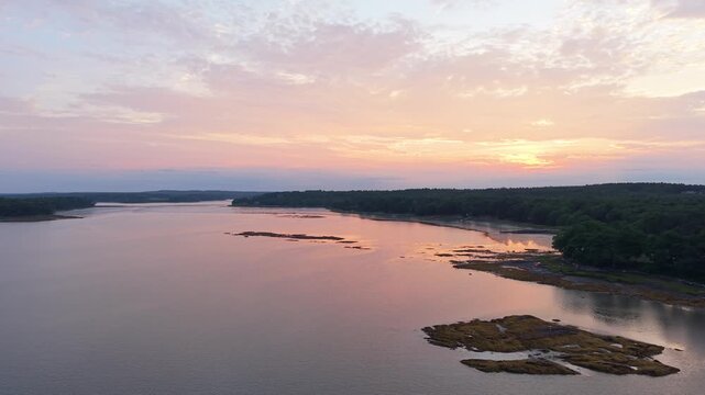 Sunset over a tranquil coastal inlet and rocky tidal marsh near Freeport, Maine, with soft pastel clouds reflecting on calm waters along Casco Bay.