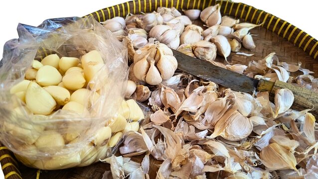 fresh peeled white garlic cloves inside a clear plastic bag positioned next to dry garlic skin husks, capturing kitchen food preparation
