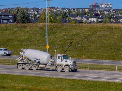 Calgary, Alberta, Canada. September 27, 2026. White concrete mixer truck driving on a multi-lane highway near suburban hillside homes.