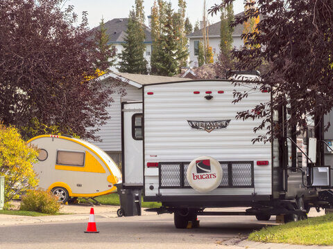 Calgary, Alberta, Canada. September 27, 2026. Recreational vehicles parked on a suburban driveway framed by trees during daylight.