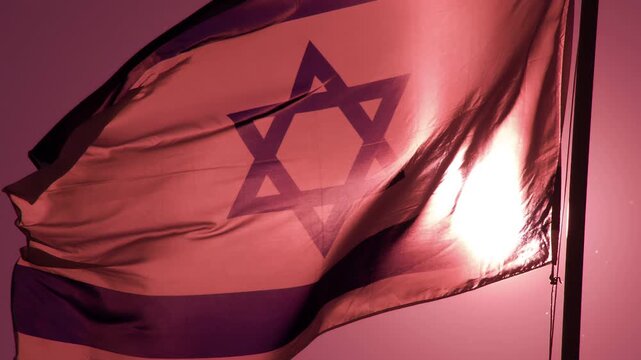 Israeli Flag in the Dawn Rays. The Big State Flag is illuminated by the sun and flutters epically in the wind against the rising sun