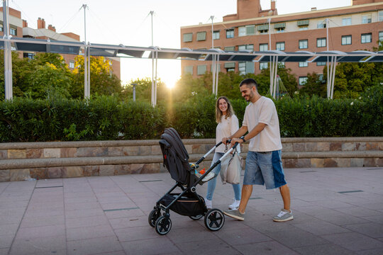 Happy family pushing stroller in urban public space at sunset