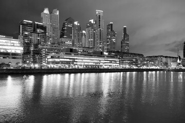 A striking black and white low-angle wide shot captures a modern urban skyline at night.  © Nataly Regina