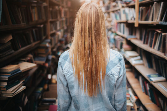 A picture og girl walking among bookshelfs with new and olb books. There is a mess everywhere in the room. She ir making a reseach.
