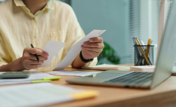 Asian Woman reviewing household bills and receipts beside a laptop at home. Personal budgeting and expense planning help manage debt, monthly payments and financial balance.