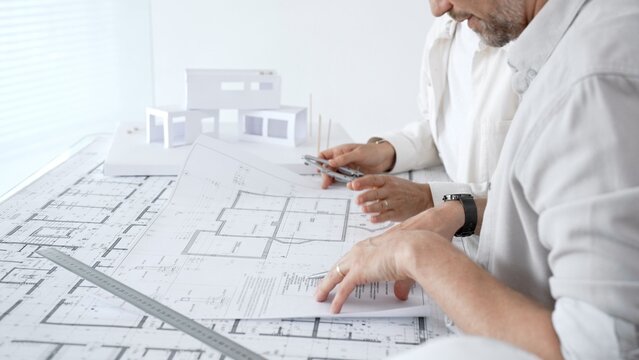 Architects and engineers collaborating on a building project, reviewing blueprints and floor plans for a new house design with a physical model