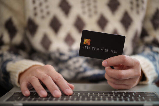 Woman holding a credit card while typing on a laptop during Christmas. Online shopping and digital payment support holiday purchases, retail sales and seasonal spending.