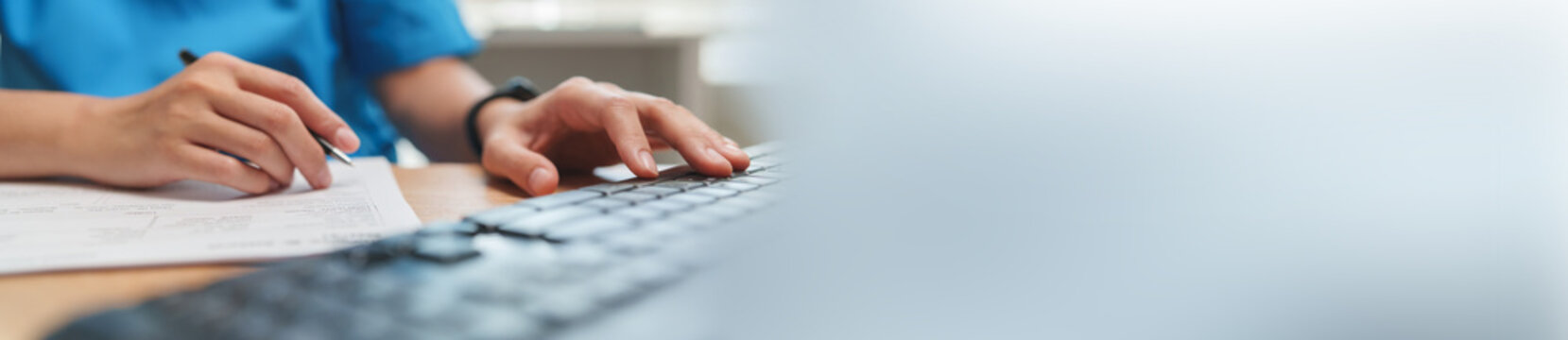 Medical professional reviewing patient documents while working at a computer. Digital healthcare supports clinical records, diagnosis, data management and patient care.