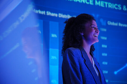Smiling businesswoman speaking at a data analytics seminar with a digital dashboard, representing presentation, business intelligence, performance metrics, finance and technology.